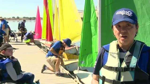 People on dock next to small sail boats.